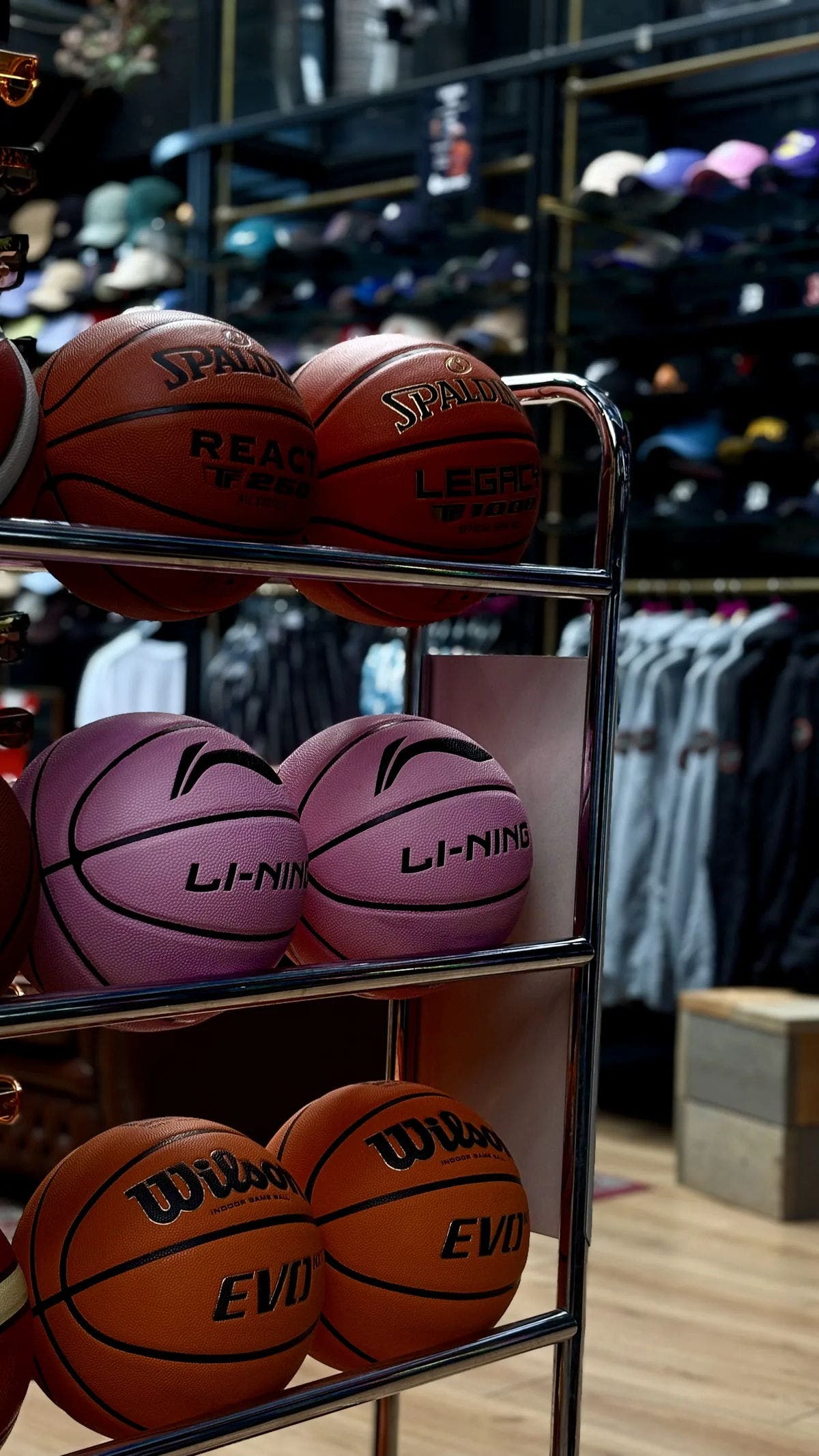Basketbalrek met Spalding-, Li-Ning- en Wilson-basketballen voor een wand met petten in de Burned Sports winkel in Den Bosch