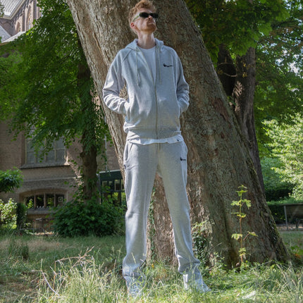 Je ziet een man met bij een boom met een joggings pak aan.