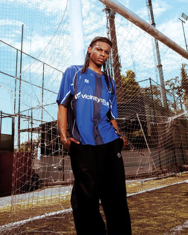 Vicinity Derby Jersey T-shirt Blauw lifestyle foto met model in buiten omgeving voetbalveld