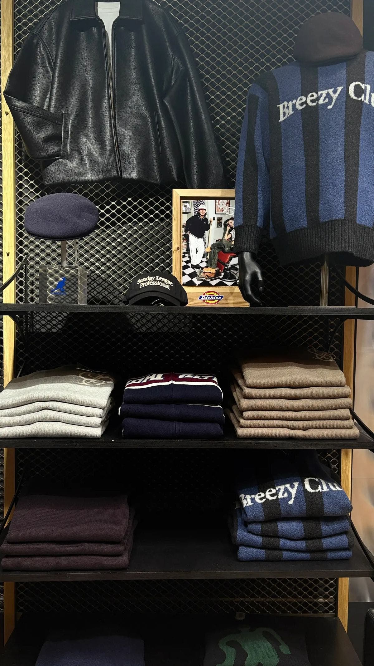 Schap met een leren jas, een gestreepte trui, petten en gevouwen truien in de winkel in Den Bosch
